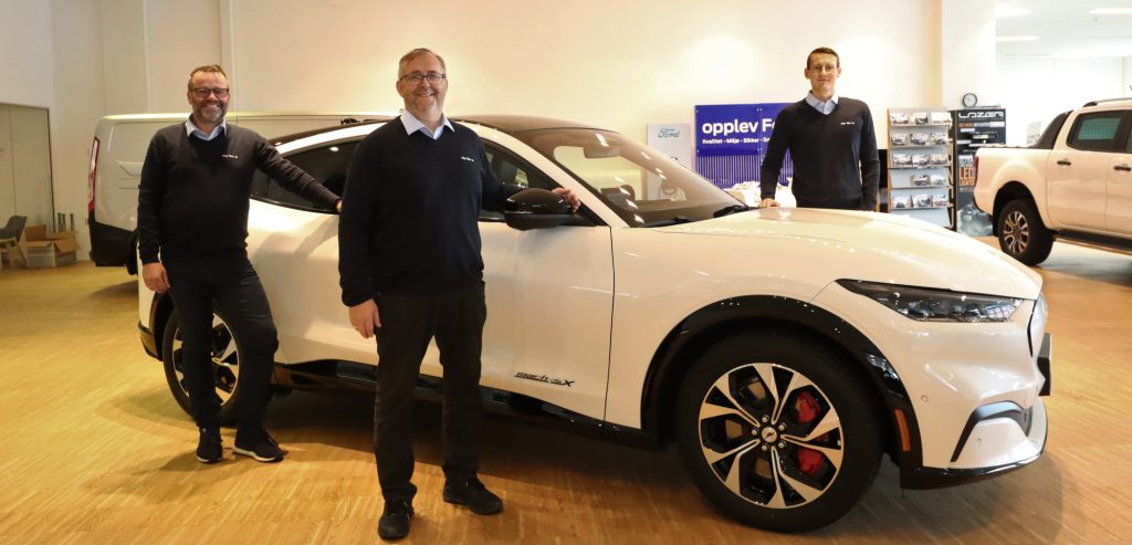 Tre mannlige bilselgere rundt en hvit bil i bilbutikk