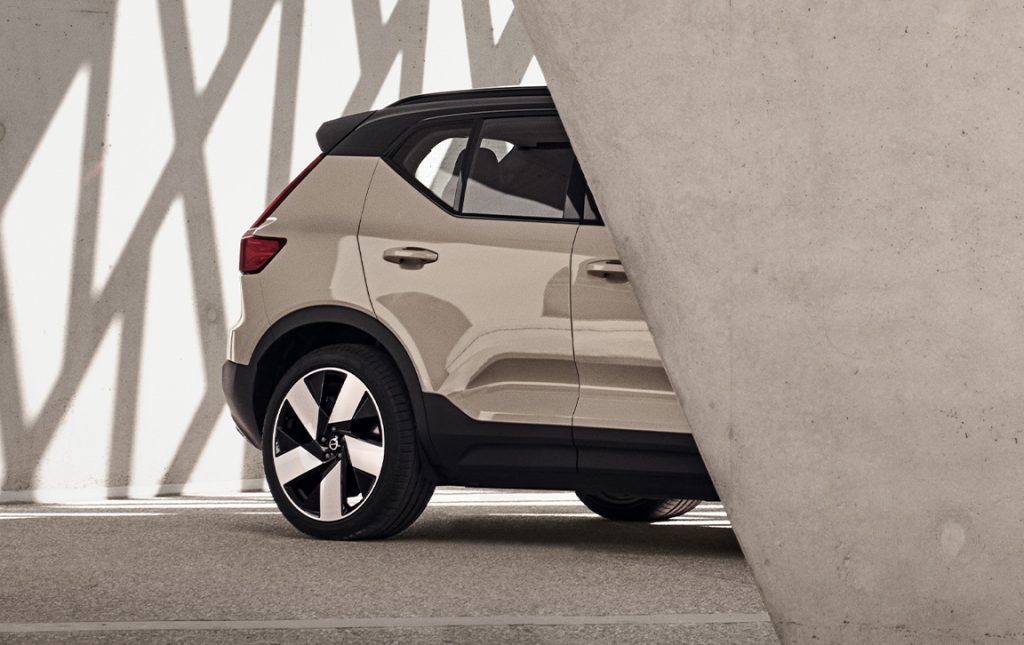 Bakenden på en sandfarget Volvo EX40 stikker frem fra bak en betongvegg, sett fra siden.